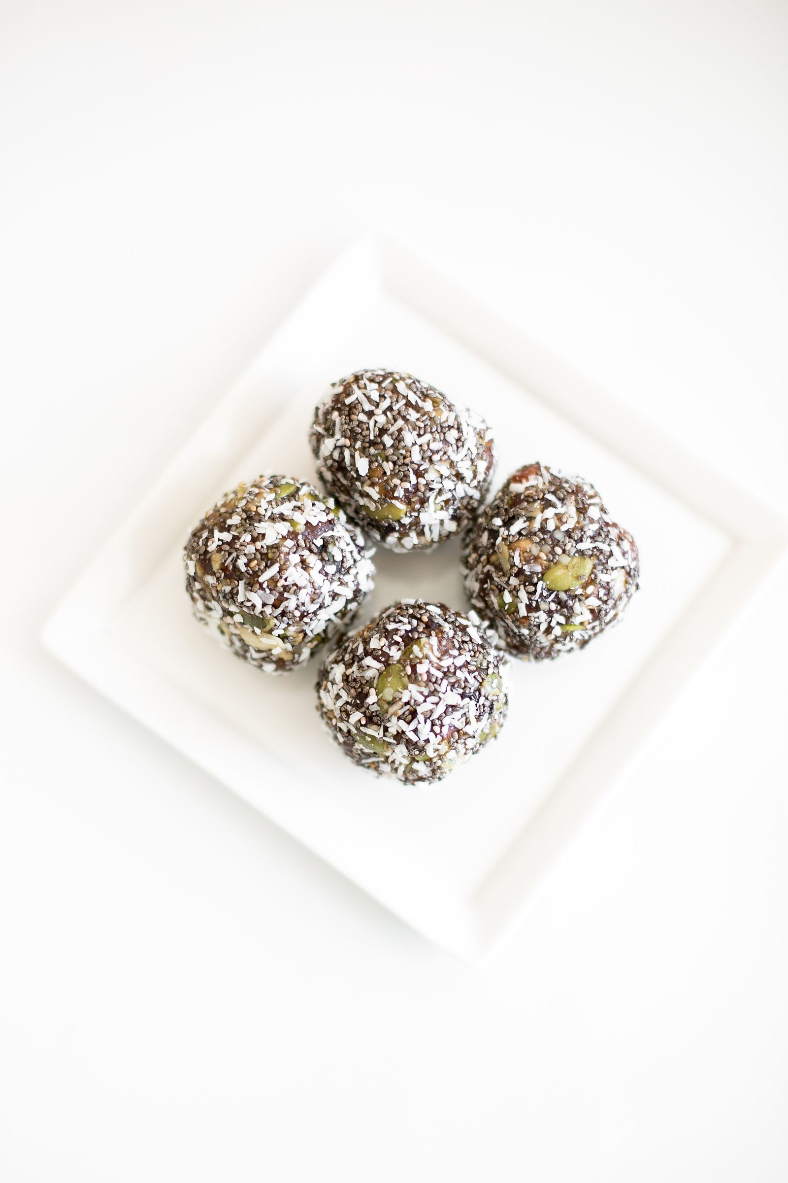 Four chia and date balls rolled in coconut with pumpkin seeds on a white plate