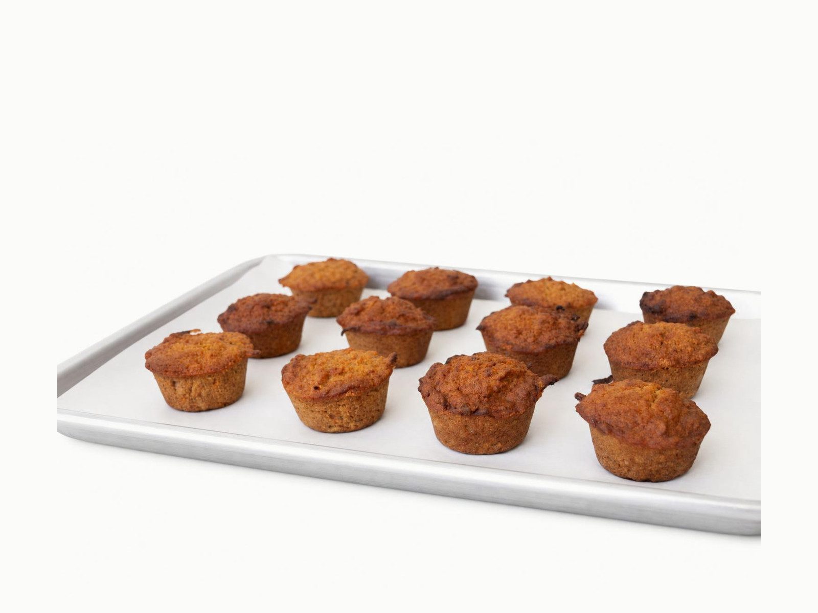 Tray of house-baked muffins, golden brown, on a white sheet pan