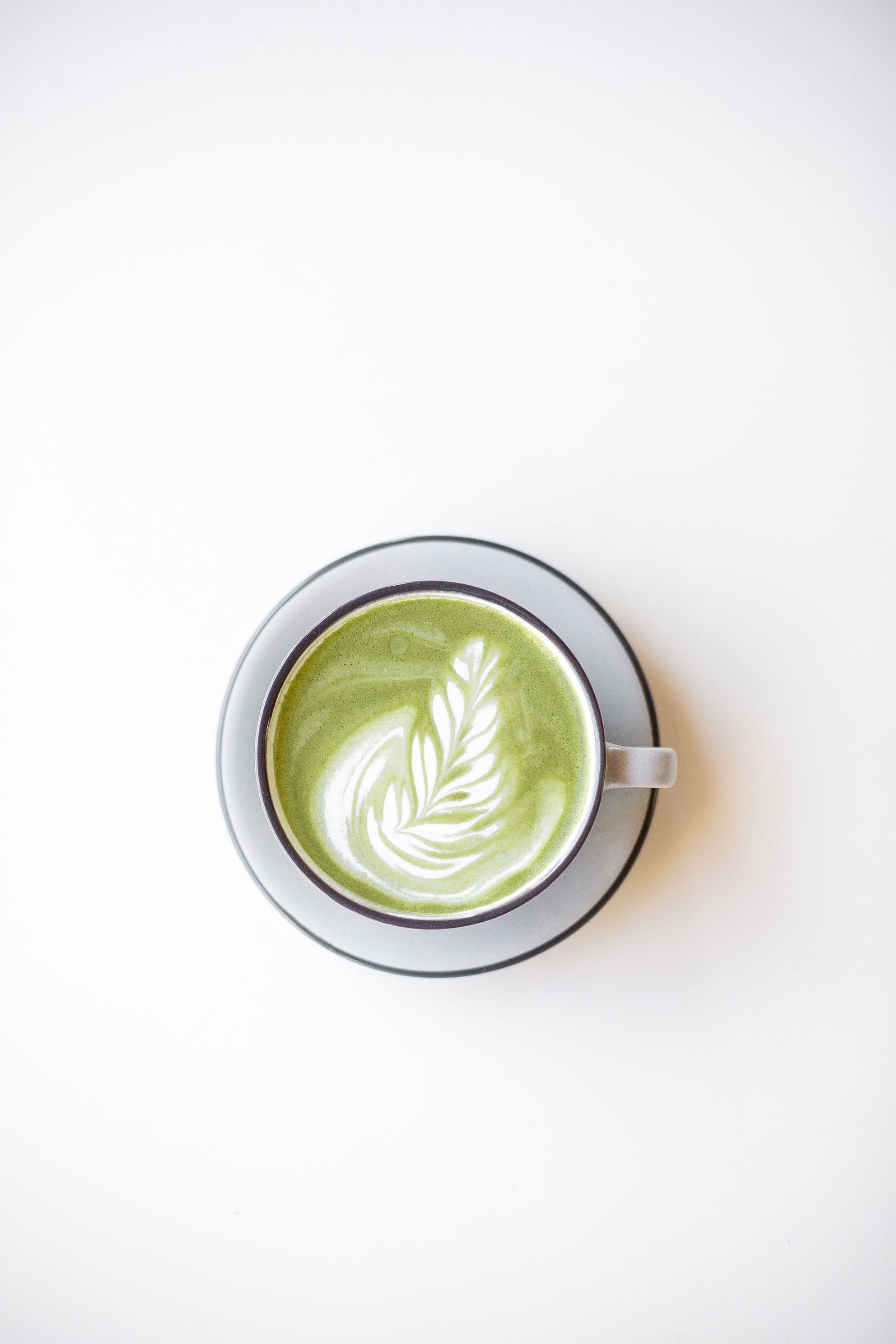 Matcha latte with rosetta foam art in a grey cup and saucer, seen from above