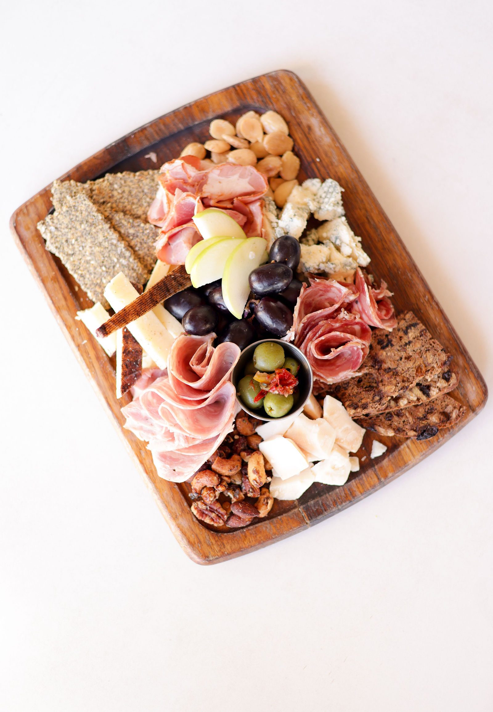 Cheese and charcuterie board with prosciutto, blue cheese, grapes, apple, olives, nuts and seeded crackers