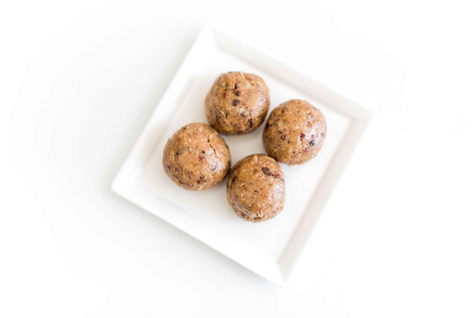 Four peanut butter power balls with oats on a white square plate