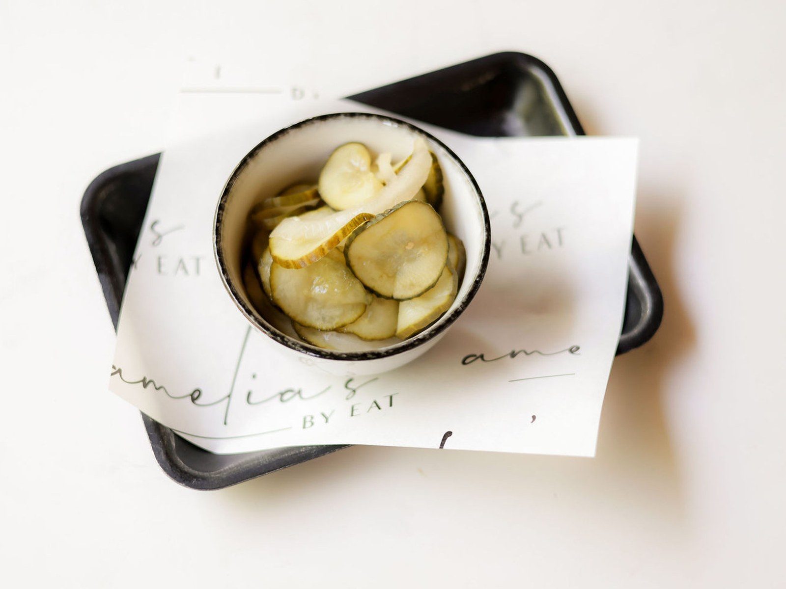 Housemade dill pickle chips in a bowl on an Amelia's branded tray