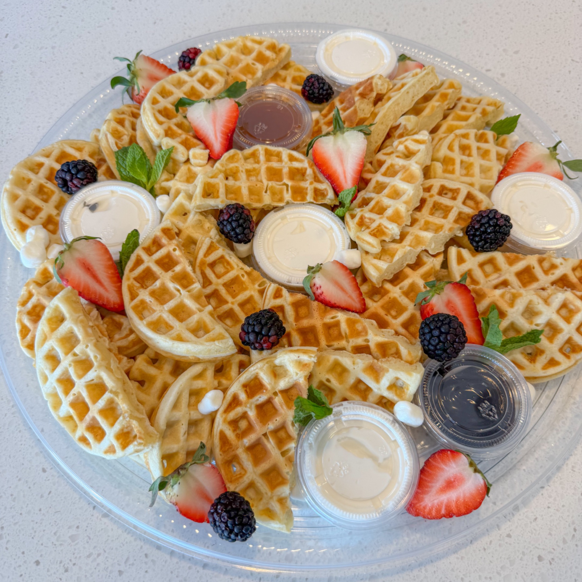 Tray of mini waffles with homemade whipped cream, caramel sauce and chocolate