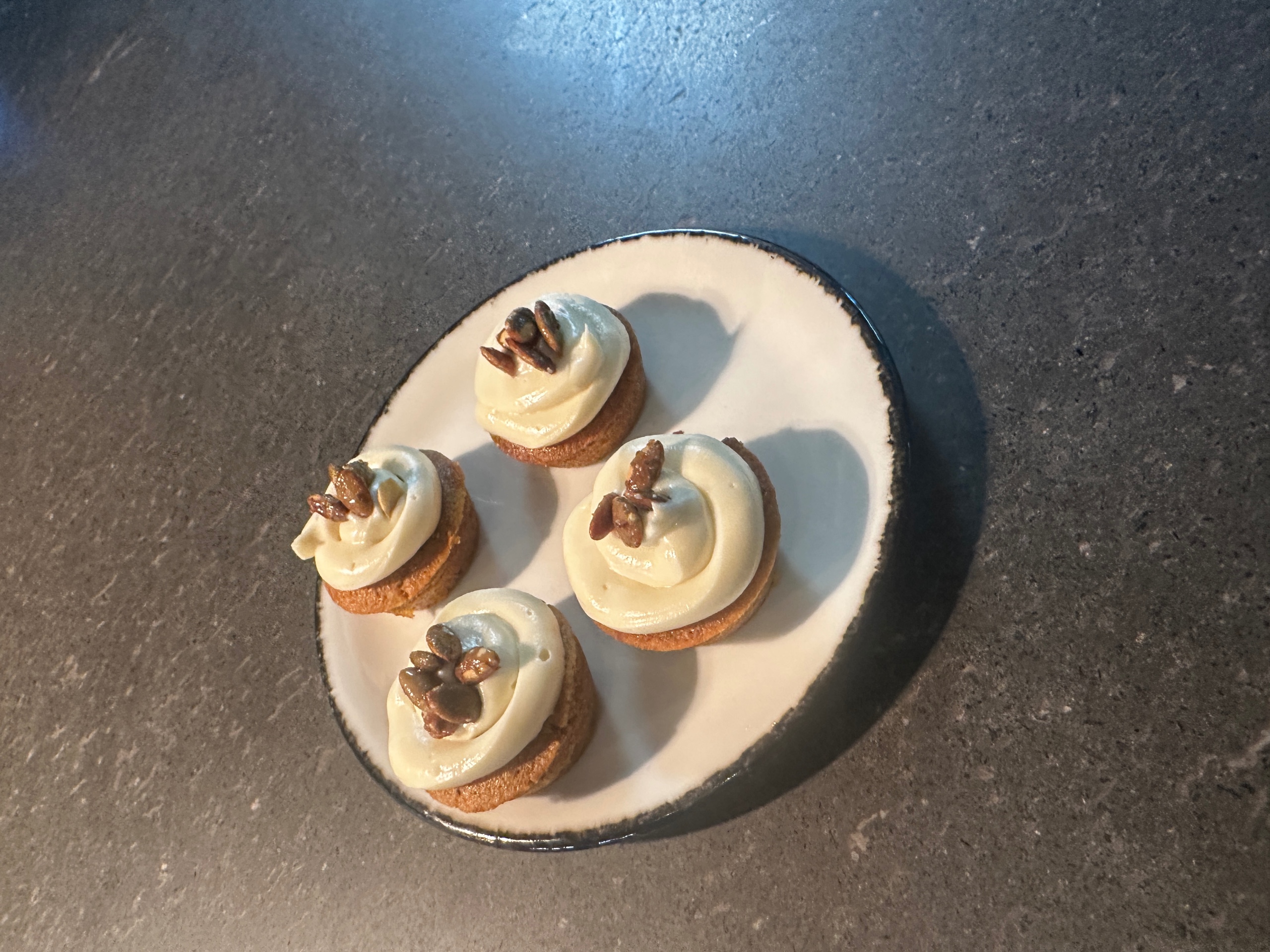 Four gluten-free pumpkin muffins with swirls of maple cream cheese frosting and toasted pumpkin seeds on a white plate