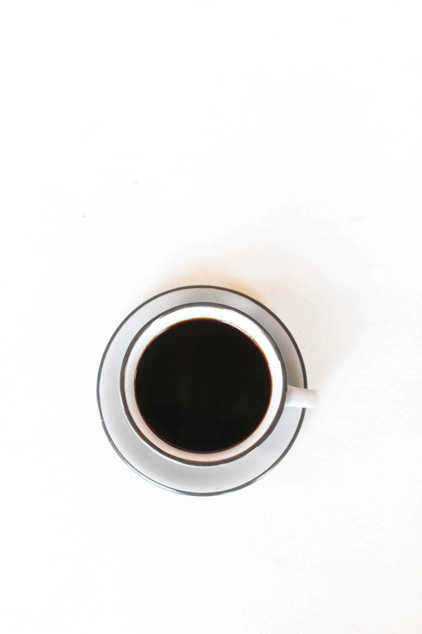 Cup of hot black drip coffee in a grey cup and saucer, seen from above