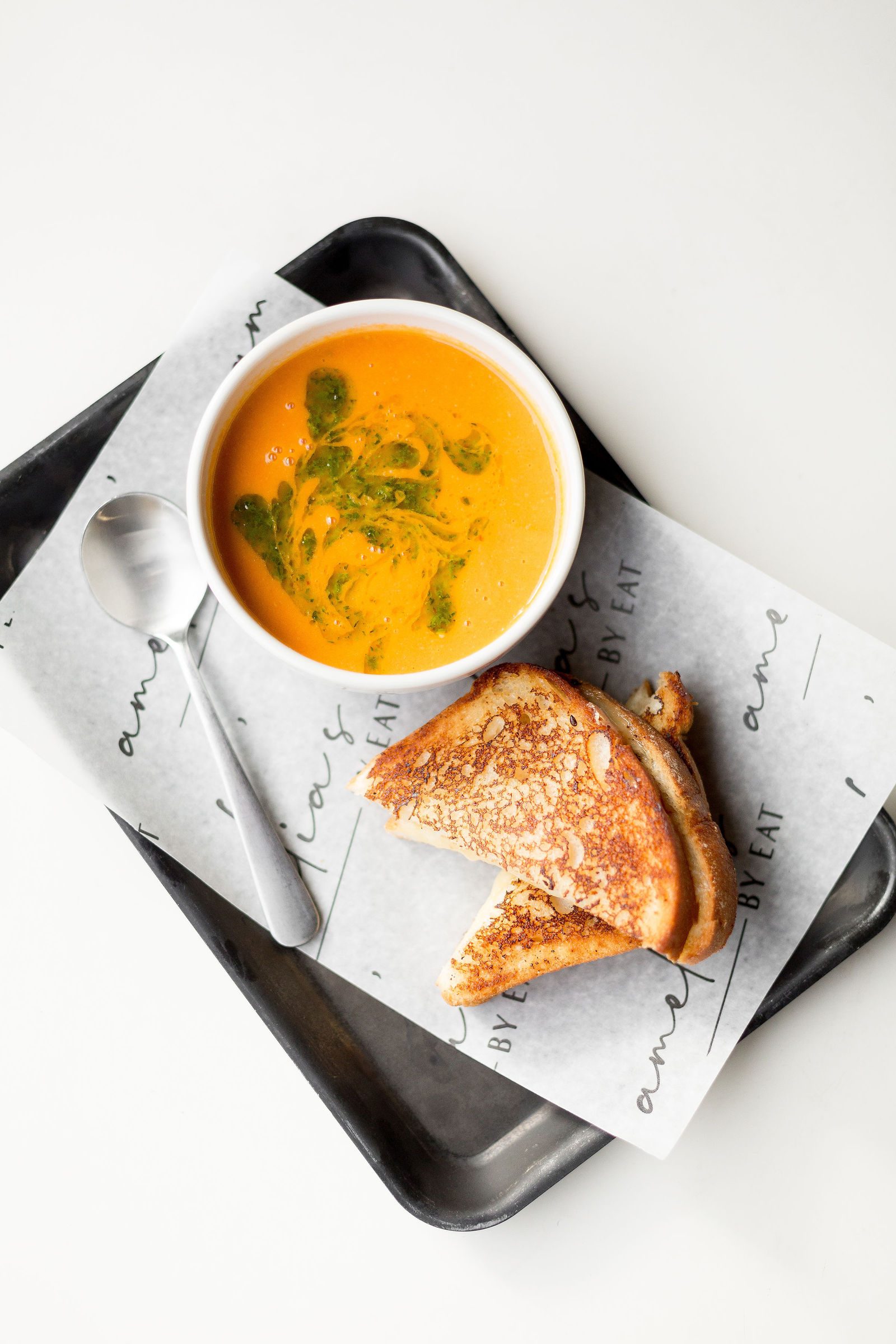 Tomato soup with a green herb swirl beside a grilled cheese sandwich on Amelia's paper