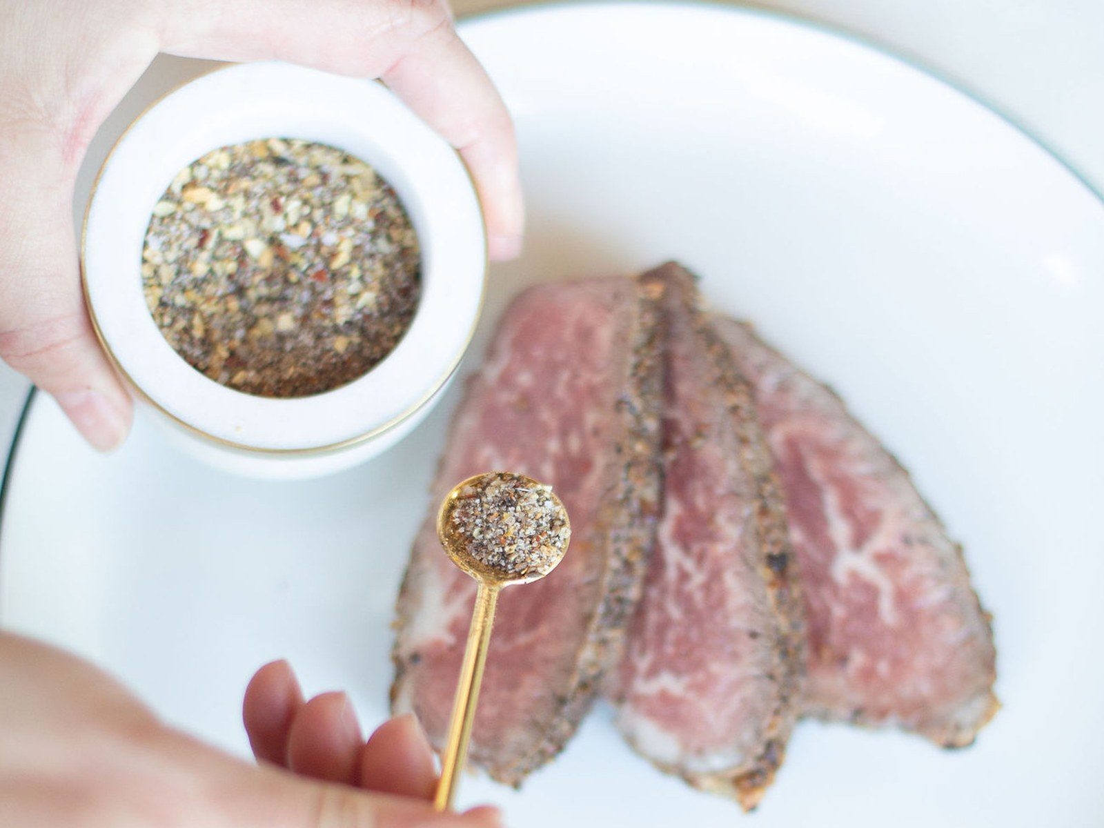 Sliced grass-fed tri-tip, pink in the middle, with a spoon of house seasoning