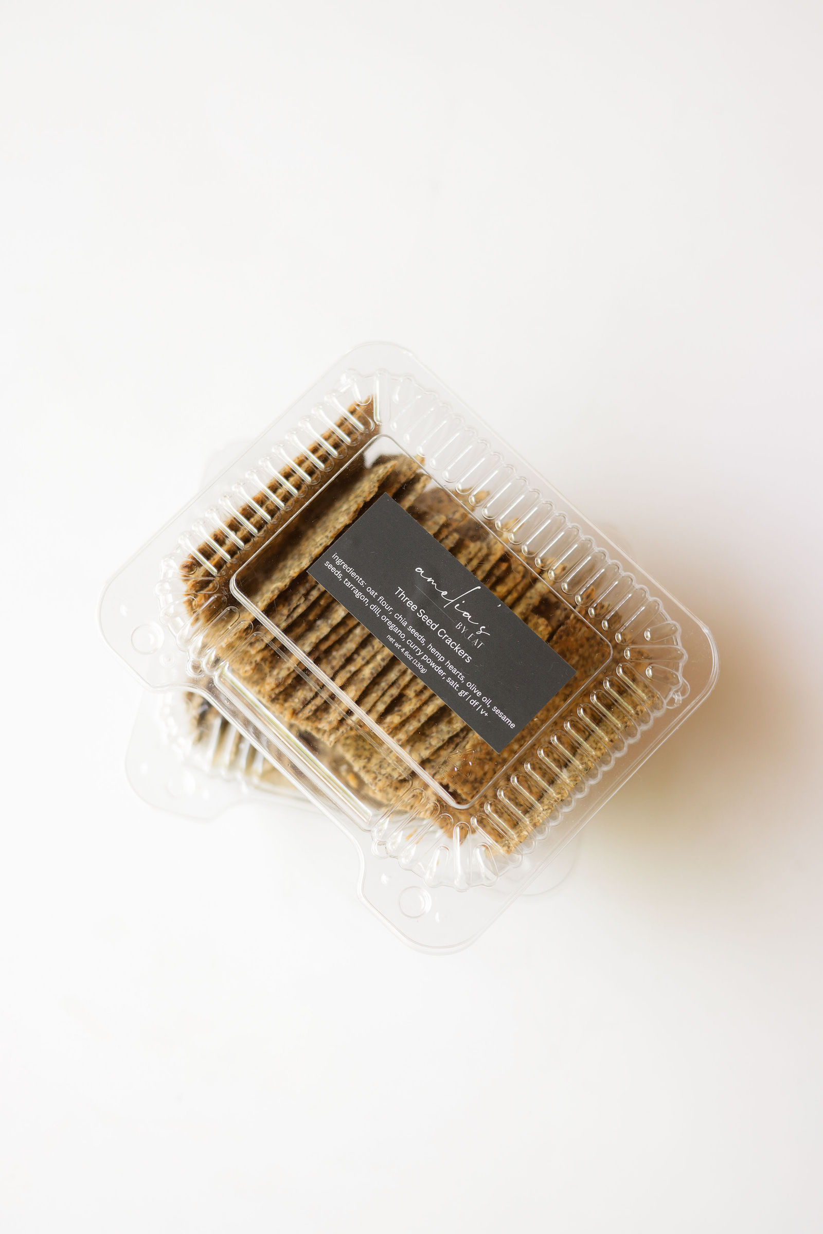 Amelia's Three Seed Crackers stacked in clear clamshell containers with a black label