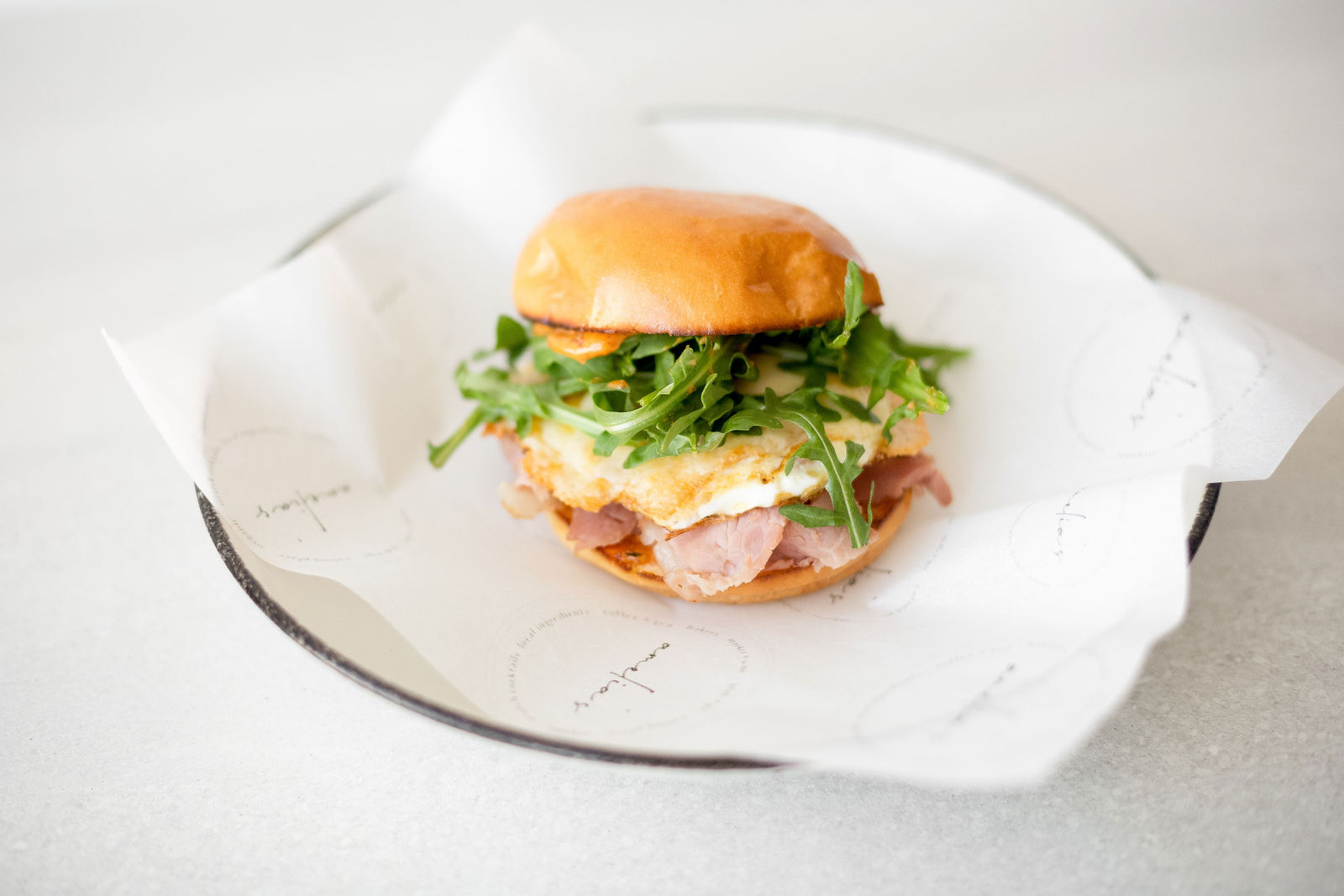 Eye Opener — fried steadfast farm egg*, shaved fra'mani ham or crispy nitrate-free bacon, arugula, calabrian chili aioli