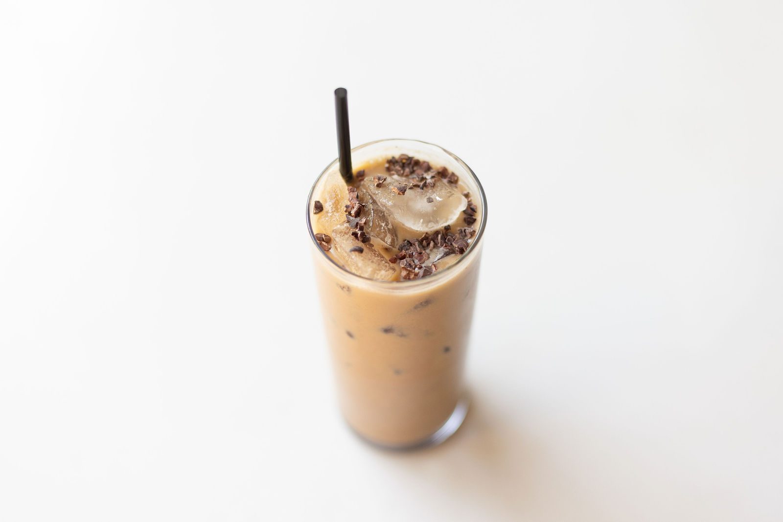 Superfood mocha over ice in a tall glass topped with crushed cacao nibs and a straw