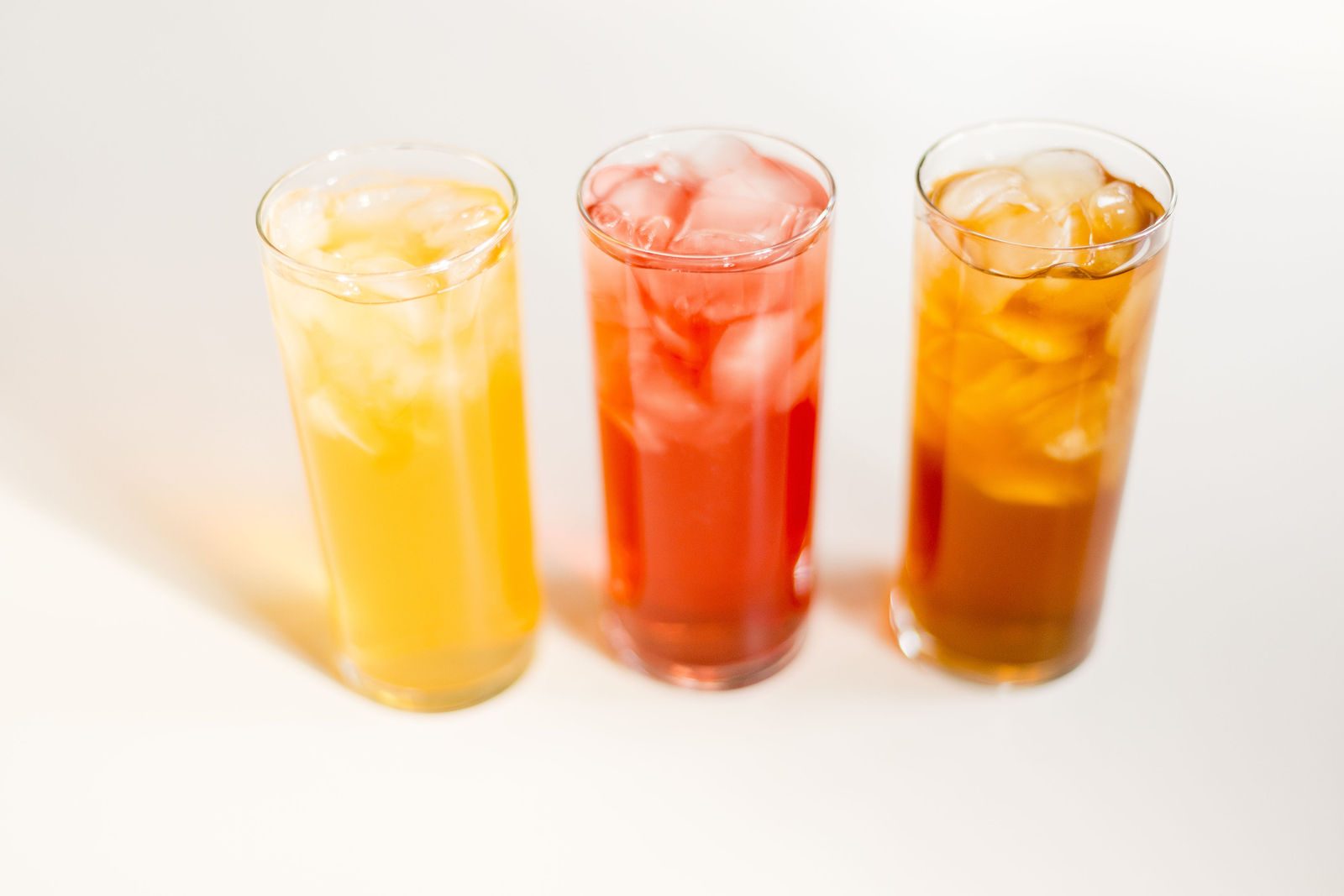 Three glasses of iced tea over ice in yellow, red and amber shades