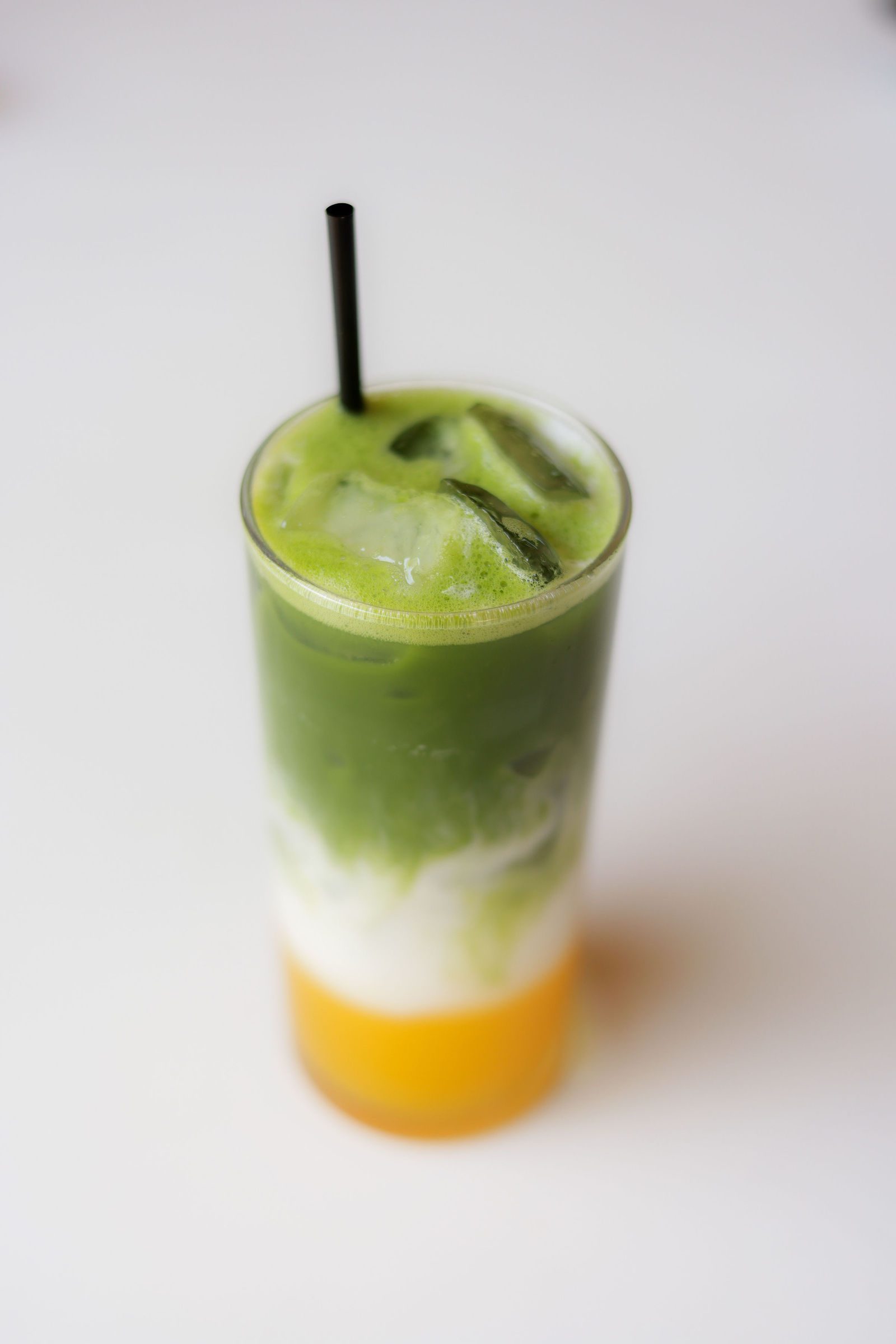 Matchacicle layered iced drink of matcha, milk and orange in a tall glass