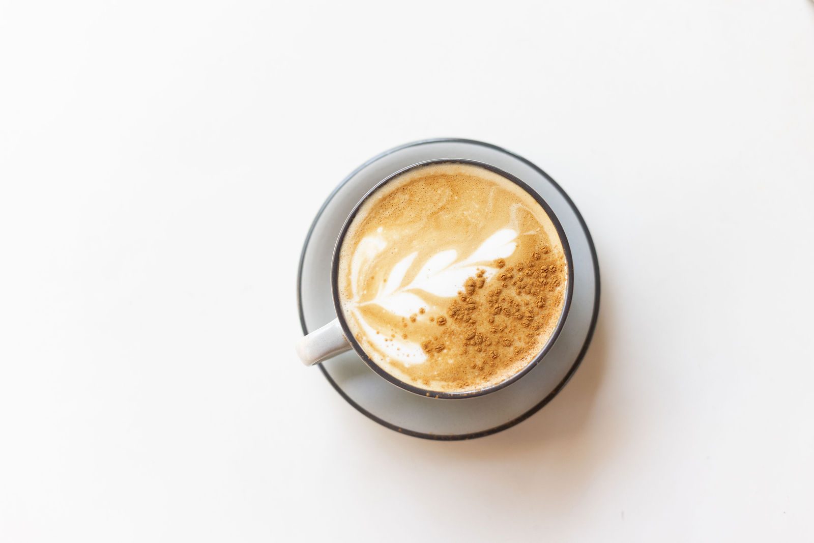 Latte with leaf latte art and a dusting of cinnamon in a grey cup and saucer