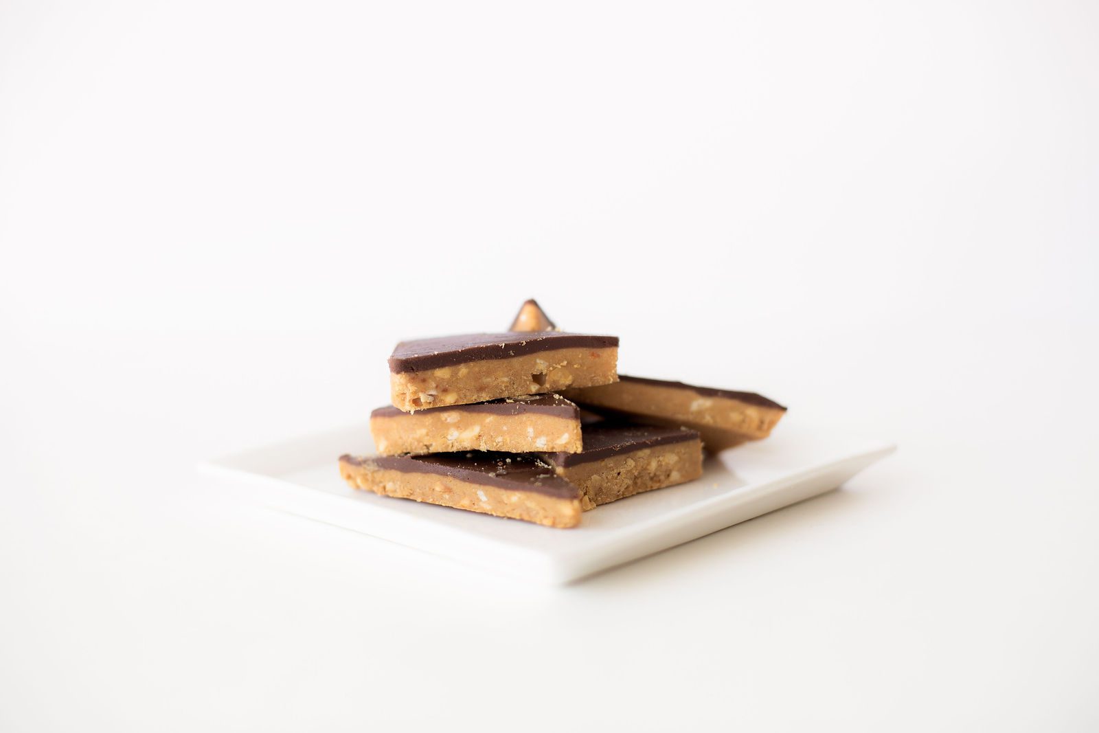 Stacked pieces of chocolate-topped peanut butter pretzel brittle on a white plate