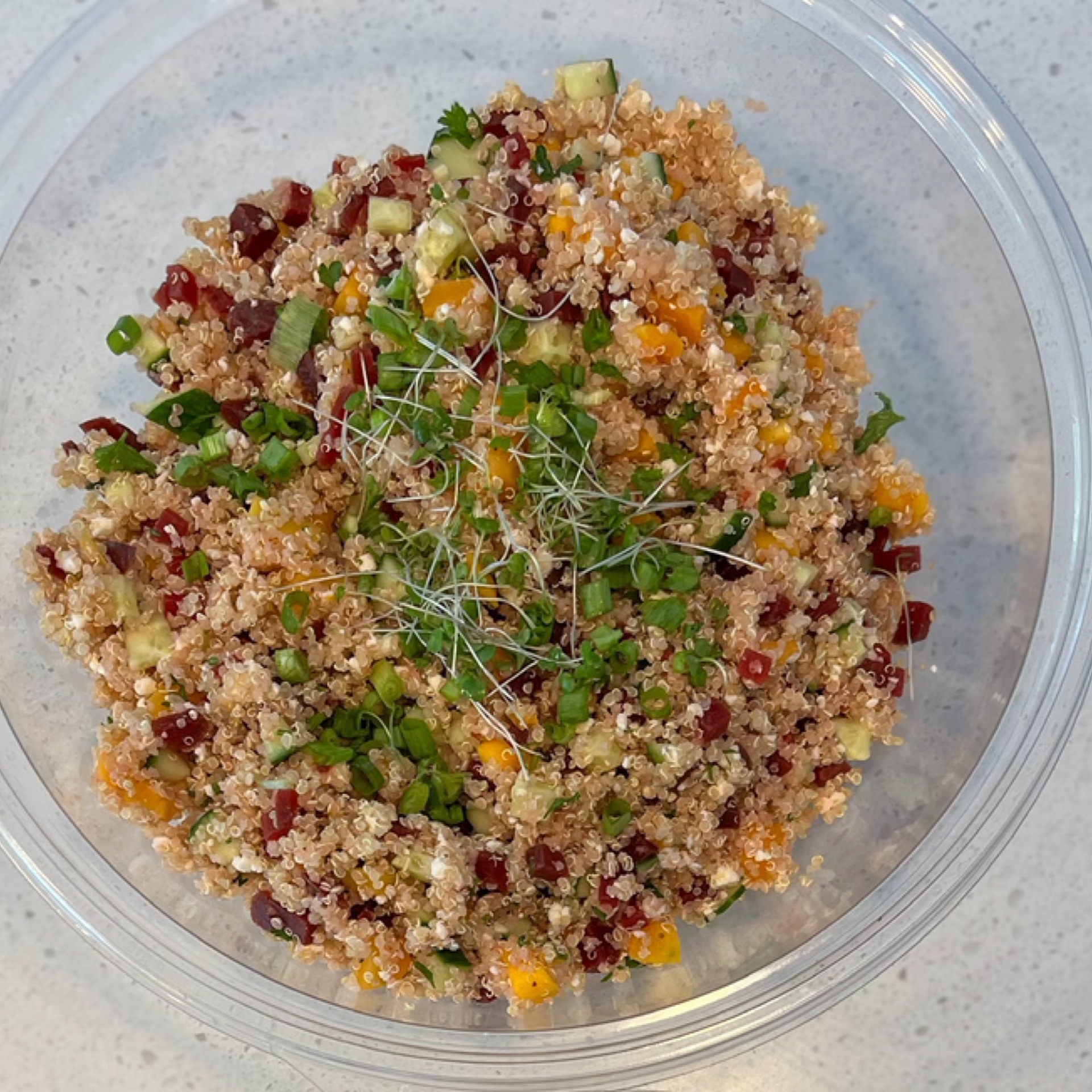 Quinoa salad bowl with cucumbers, cranberries, toasted almonds, blueberries, feta cheese, and creamy maple dressing